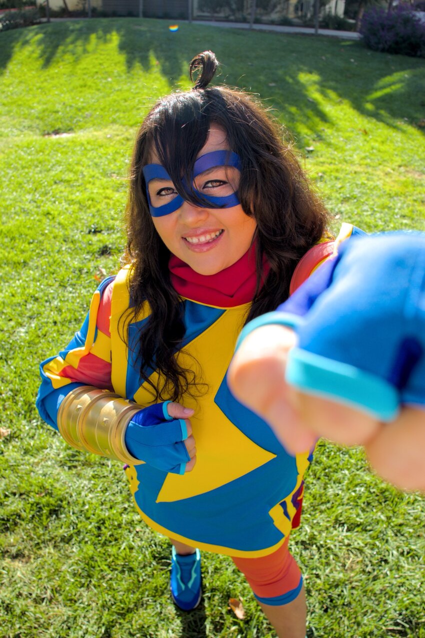 1girl blue_gloves blue_shoes brown_hair cosplay cosplay_photo female_focus fingerless_gloves gloves grass hair_between_eyes highres kryrayne looking_at_viewer marvel marvel_tokon:_fighting_souls ms._marvel ms._marvel_(cosplay) outdoors photo_(medium) shoes smile solo superhero_costume teeth