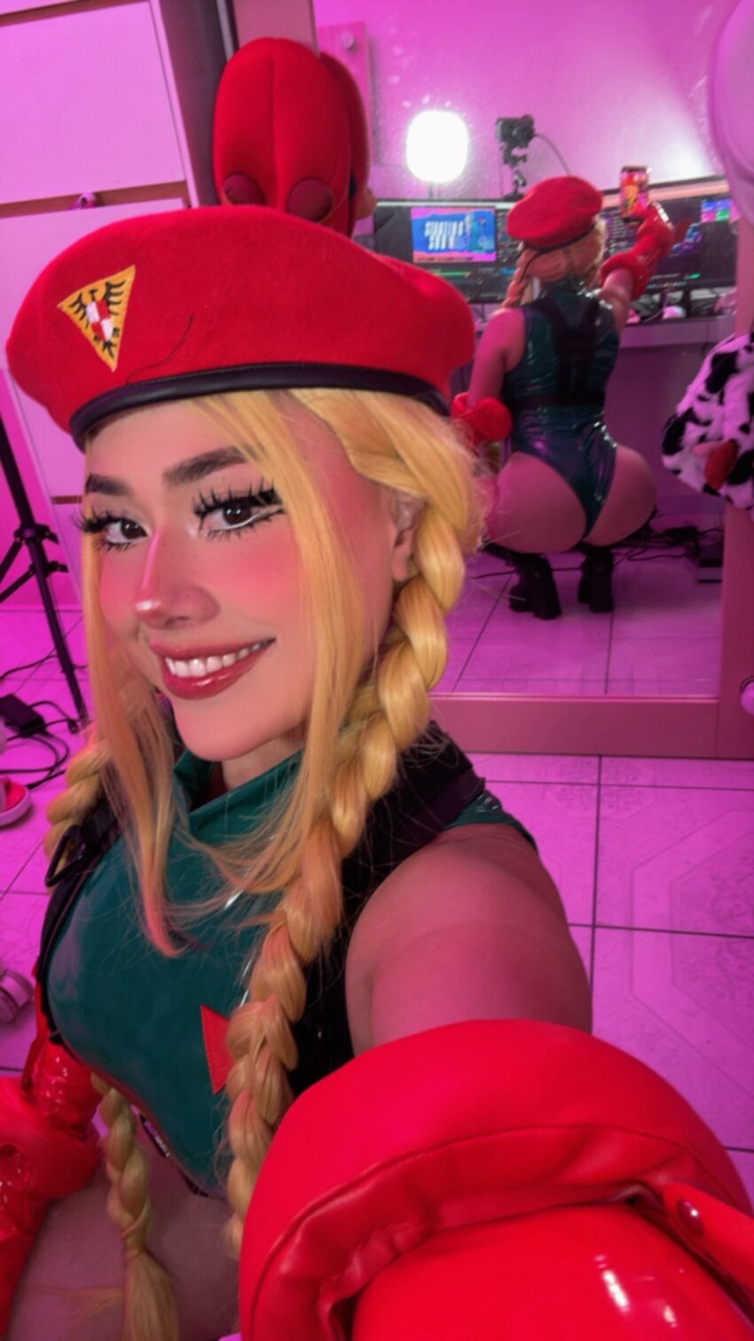 1girl ass ass_shake bare_shoulders blonde_hair braid breasts cammy_white cammy_white_(cosplay) cosplay curvy fingerless_gloves full_body gloves green_leotard hat highleg highleg_leotard highres huge_ass leotard long_hair looking_at_viewer looking_back magsmx mexican_(nationality) mirror mirror_selfie monitor parted_lips real_life revealing_clothes selfie shiny_clothes shiny_skin smile squatting street_fighter thong_leotard twerking twin_braids wide_hips